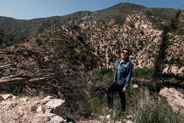 A brunette woman in a jean jacket stands out in chapparal hills.